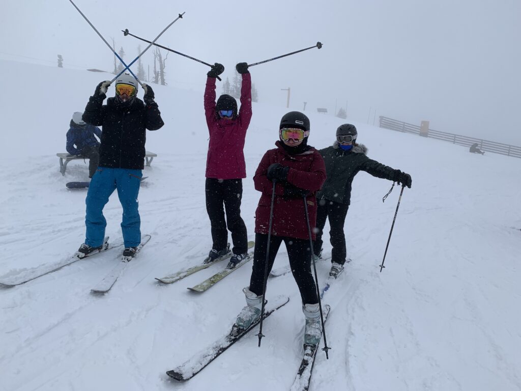 4 people on skis with poles in the air excited and having fun